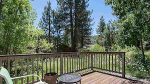 A wooden deck with a metal table and a green chair, surrounded by trees and a wooden fence.