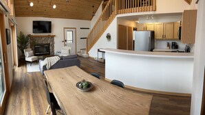 Un interior moderno con una mesa de comedor de madera, una cocina con armarios de madera y una escalera que sube a un nivel superior.