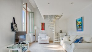A modern living room with a glass coffee table, white sofas, a spiral staircase, and a painting of a beach scene. - Appartement Perrissol - Welkeys (Cannes)