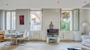 A modern living room with a dining area, large windows, a flat-screen TV, and a radiator. - Appartement Perrissol - Welkeys (Cannes)