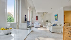 A spacious living area with a white sofa, a dining table with a bowl of fruit, and a spiral staircase. - Appartement Perrissol - Welkeys (Cannes)