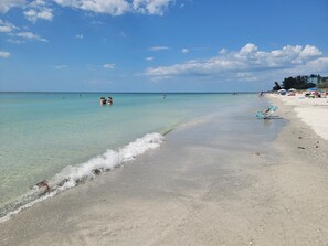 Une plage avec une eau turquoise et limpide, un rivage sablonneux et quelques personnes au loin.