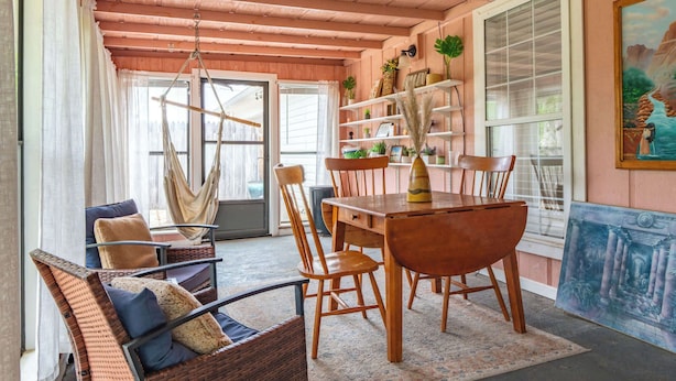 Una stanza con soffitto in legno, un tavolo da pranzo con sedie, un'amaca e una libreria con diversi oggetti.
