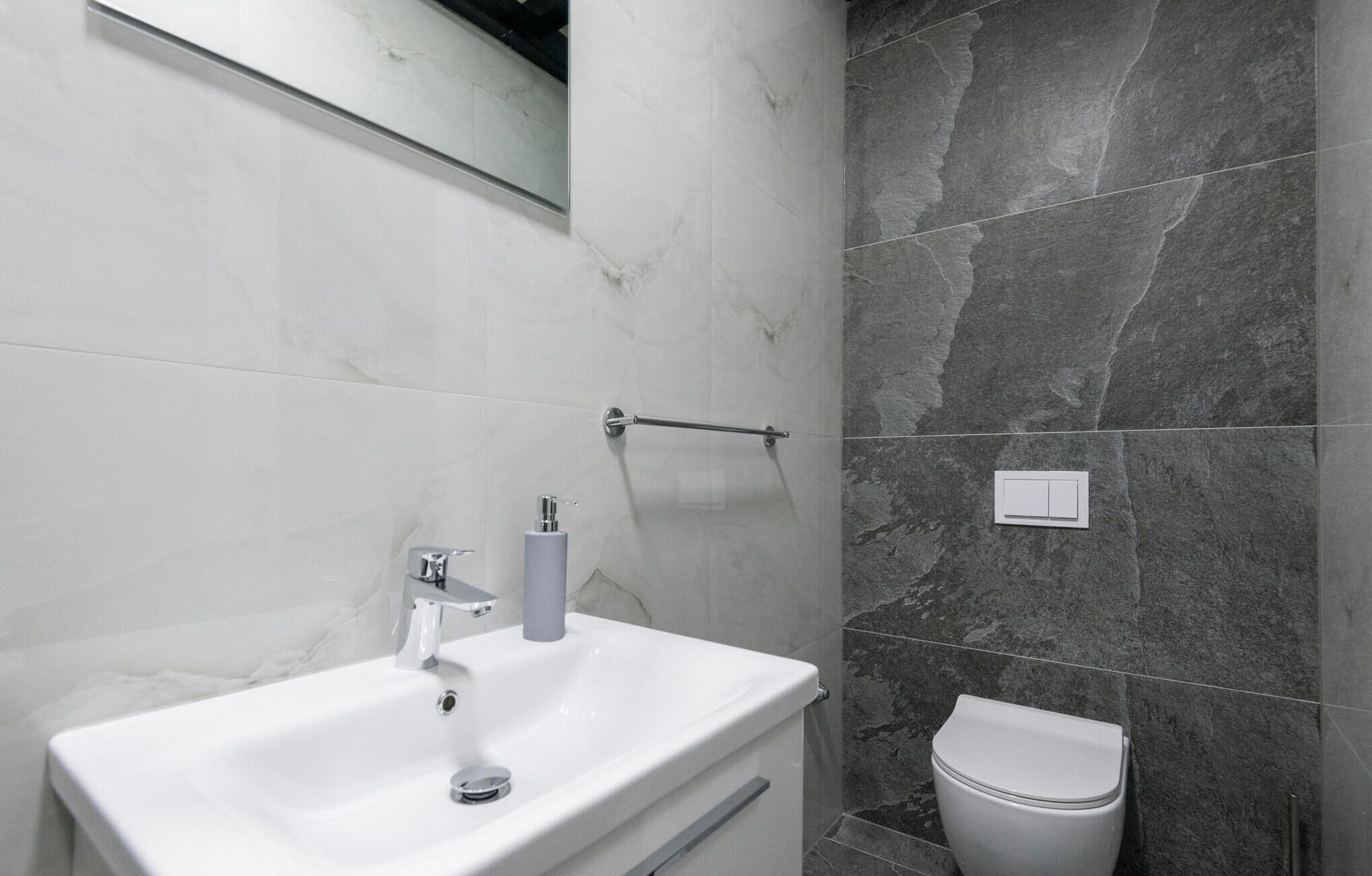 A bathroom with a white sink, a mirror, a towel rack, a toilet, and a shower area with dark stone tiles.