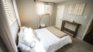 A neatly made bed with white linens, a bedside table with a tissue box, and a wall-mounted artwork. - Basecamp Denver 2BR Guest Suite near Red Rocks (Lakewood)