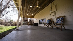 An outdoor covered patio area with concrete flooring, wooden chairs, and a ceiling fan. - Basecamp Denver 2BR Guest Suite near Red Rocks (Lakewood)