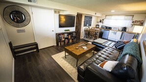 A living room with a sofa, coffee table, bookshelf, and a television. - Basecamp Denver 2BR Guest Suite near Red Rocks (Lakewood)