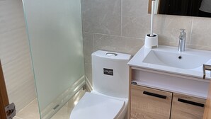 Een moderne badkamer met een douchecabine van glas, een wit toilet en een wastafel met spiegel erboven.