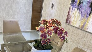 Een modern interieur met een tafel met glazen blad, omringd door stoelen met kussens, een decoratieve orchidee en een textuurmuur met een kleurrijk abstract schilderij.
