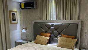 Een moderne slaapkamer met een groot bed, een gestoffeerd hoofdeinde en een nachtkastje met een lamp.