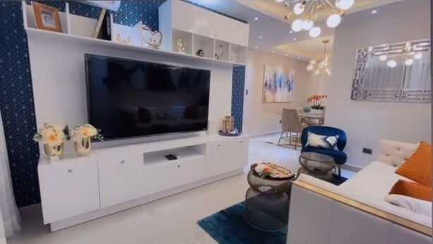 Een moderne woonkamer met een grote flatscreen televisie, witte kasten en decoratieve objecten.