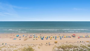 Una playa con hileras de sombrillas y sillas de playa de colores, una torre de salvavidas y una orilla arenosa.