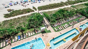 Un resort con zona de piscina, sillas de descanso y sombrillas en la playa.
