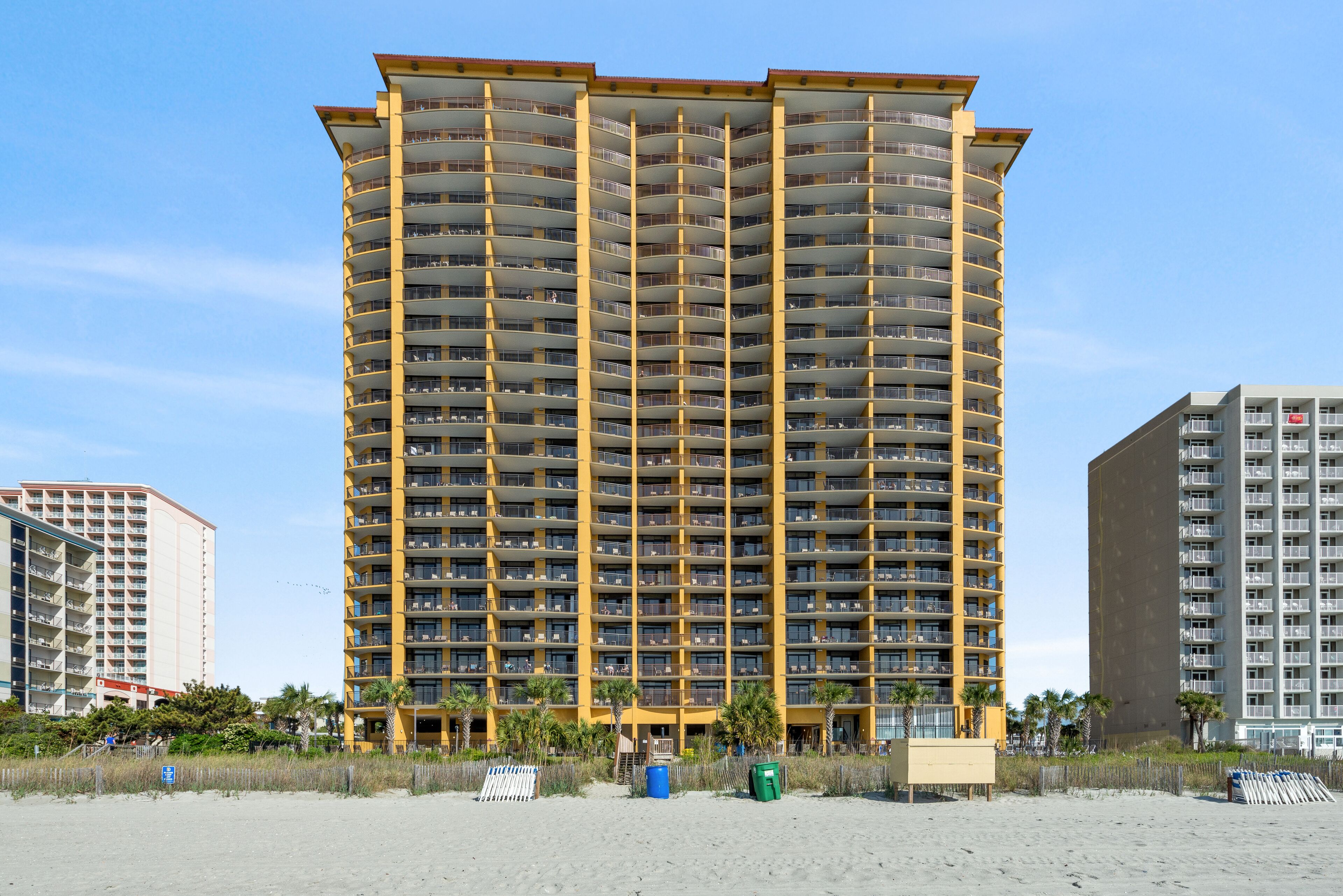 A high-rise hotel with multiple balconies, located adjacent to a beach.