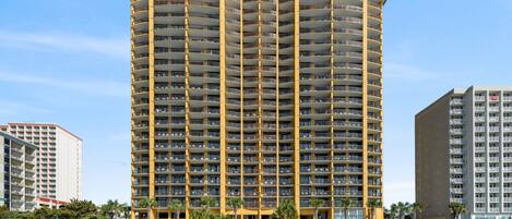 A high-rise hotel with multiple balconies, located adjacent to a beach.