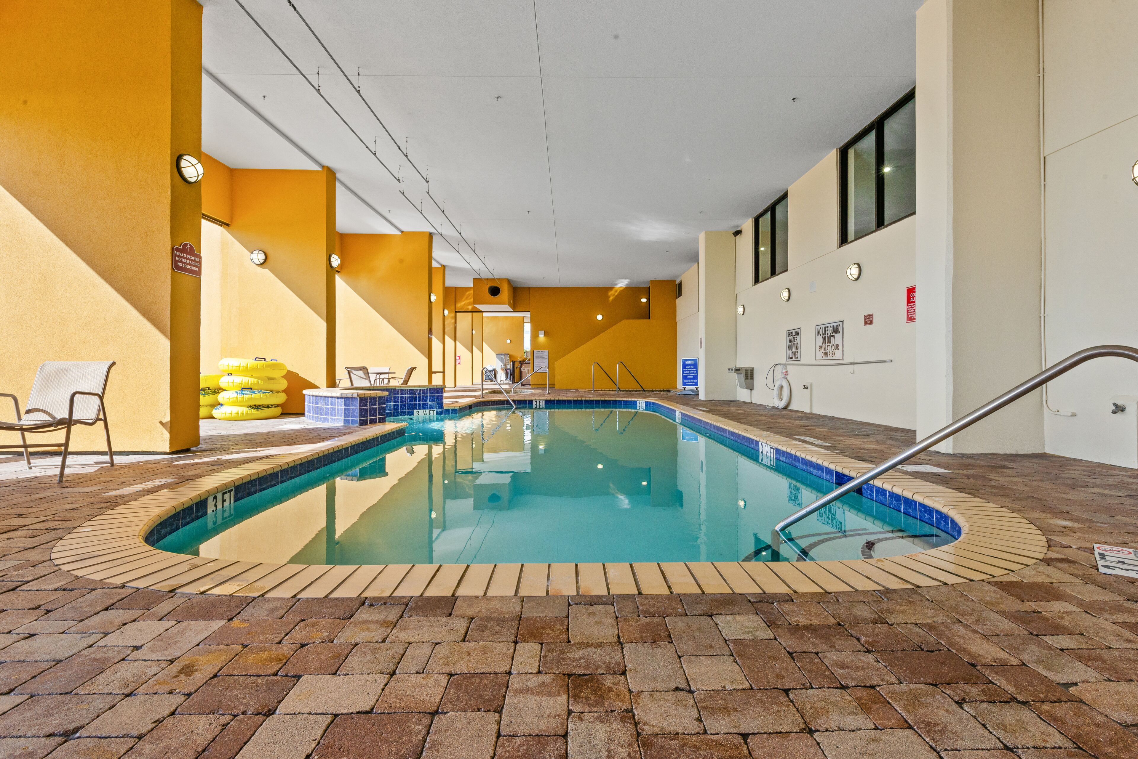 An indoor swimming pool with a tiled edge, surrounded by a brick floor, and yellow walls.