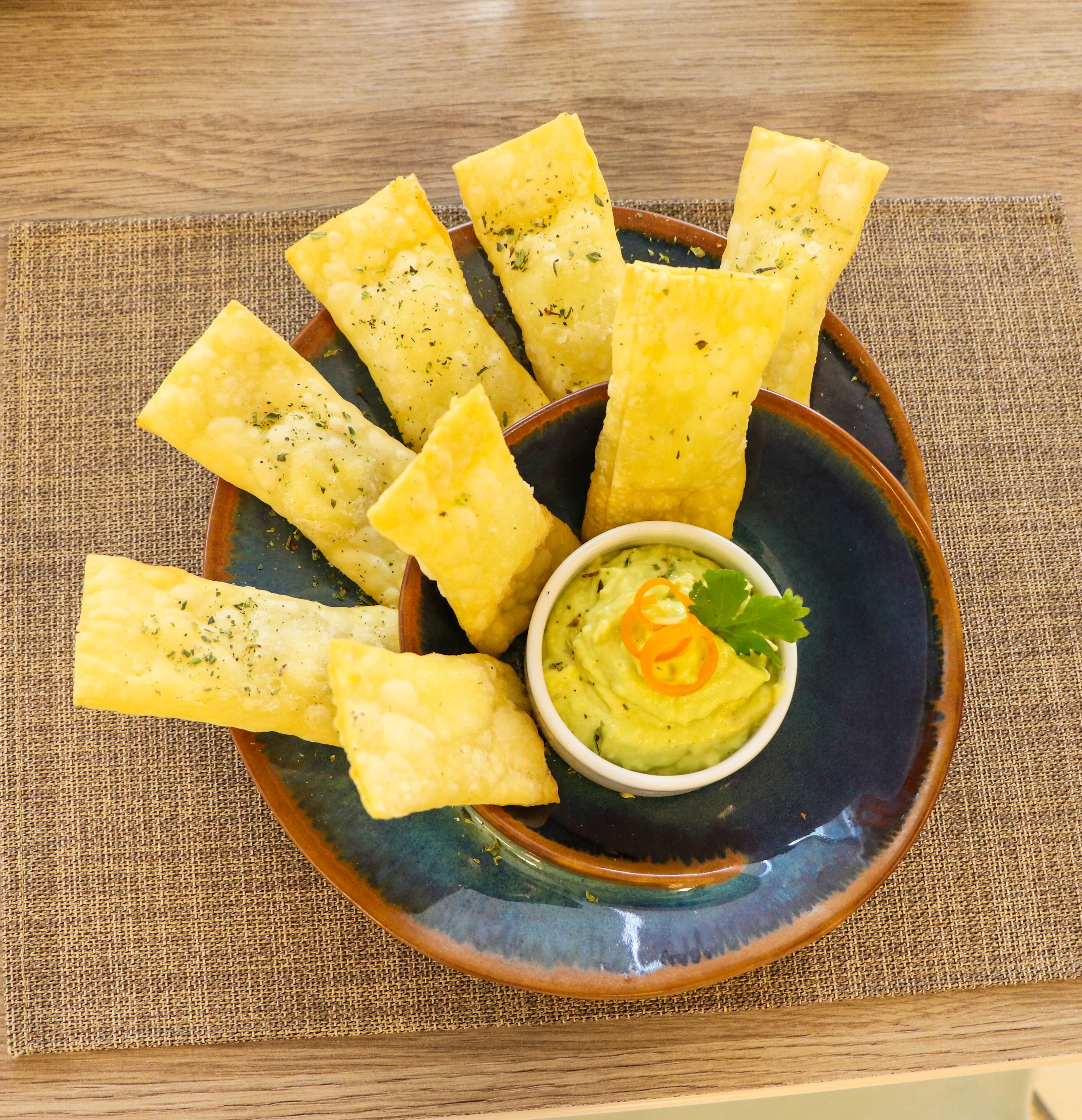A plate of fried breadsticks with a bowl of green dip in the center.