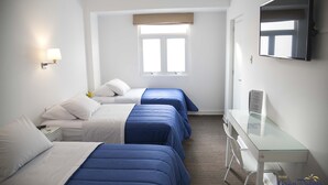 Habitación de hotel con tres camas, un escritorio, una silla, un televisor y una ventana con vistas.