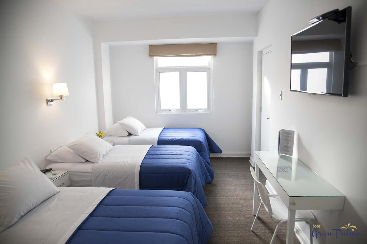 Ein Hotelzimmer mit drei Betten, einem Schreibtisch, einem Stuhl, einem Fernseher und einem Fenster mit Blick.