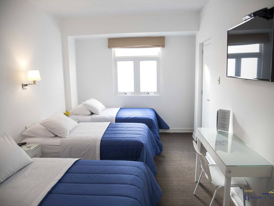 Una camera d'albergo con tre letti, una scrivania, una sedia, una televisione e una finestra vista.