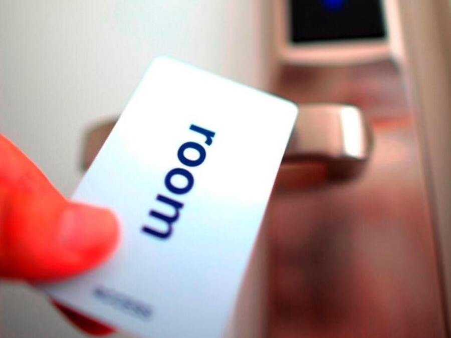 A hand holding a card with the word "room" on it, in front of a door with a digital lock.