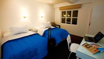 A hotel room with two beds, a desk with a laptop, and a window with curtains.