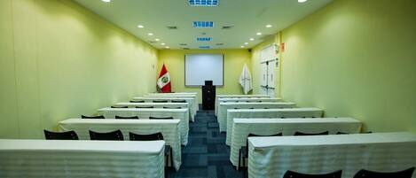 A conference room with rows of tables and chairs, a projector screen, and a podium at the front.