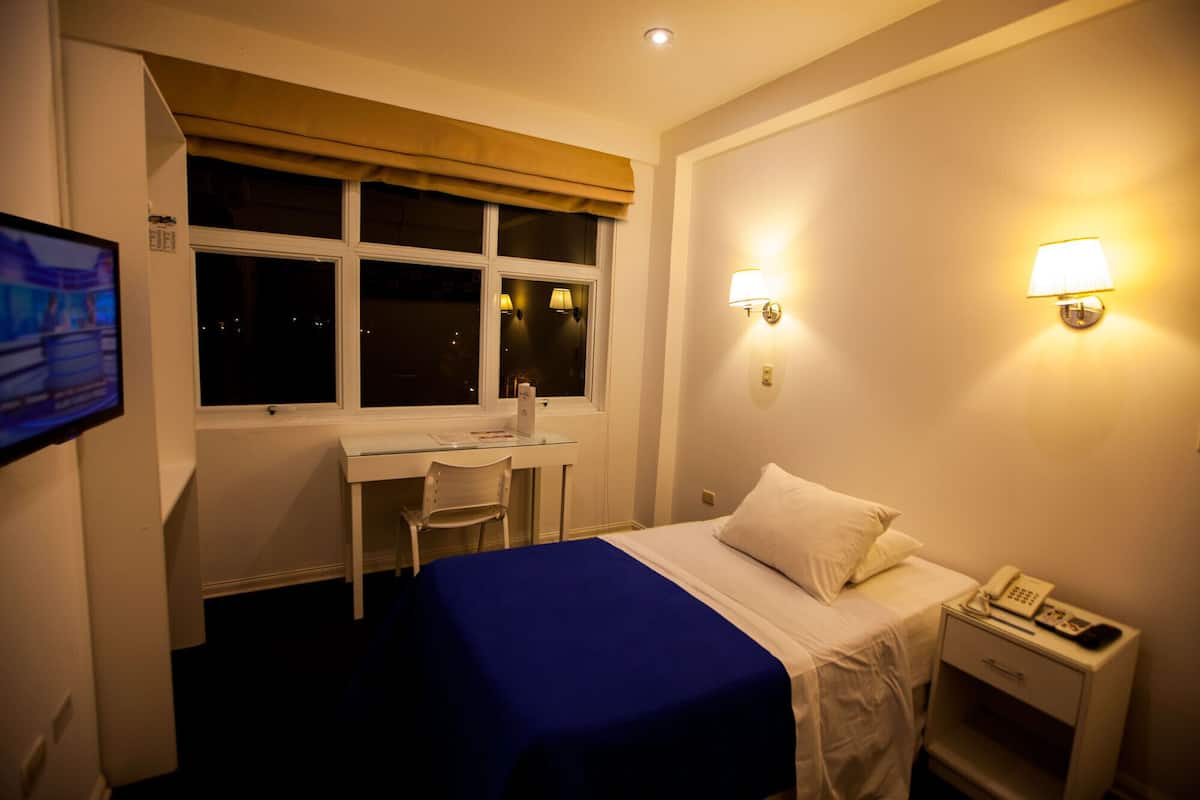 Ein Hotelzimmer mit Bett, Schreibtisch, Stuhl und zwei Wandleuchten.