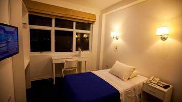 Une chambre d’hôtel équipée d’un lit, d’un bureau, d’une chaise et de deux lampes fixées au mur.