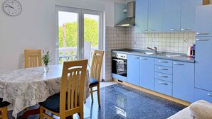 Cocina compacta con armarios azules, una mesa de comedor con sillas, un reloj en la pared y vistas a través de la puerta.