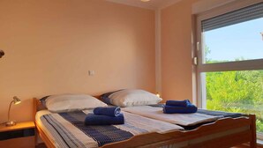 Una cama doble con ropa de cama a rayas, una mesita de noche con lámpara y una ventana con vistas al verdor.