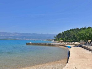 A coastal scene with a clear blue sea, a pebbly beach, and a pier extending into the water. - Holiday apartment with balcony and air conditioning (Soline)