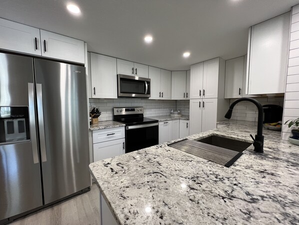 A modern kitchen with white cabinets, stainless steel appliances, a granite countertop, and a black faucet.