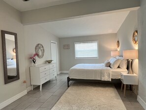 A bedroom with a bed, dresser, mirror, and a window with blinds.