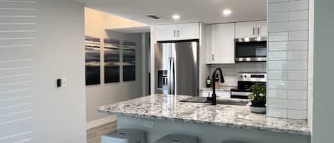 Una cocina moderna con encimera de mármol, electrodomésticos de acero inoxidable y armarios grises claros.