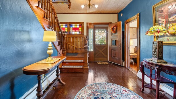 Una escalera de madera con un candelabro, una mesa de madera con una lámpara y una alfombra estampada.