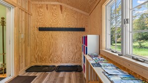 Una habitación con paneles de madera, un banco de madera, una ventana con vistas a follaje y un estante en la pared con revistas.