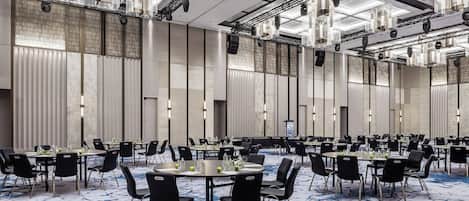 A large conference room with multiple tables and chairs, equipped with overhead lighting and a patterned carpet.