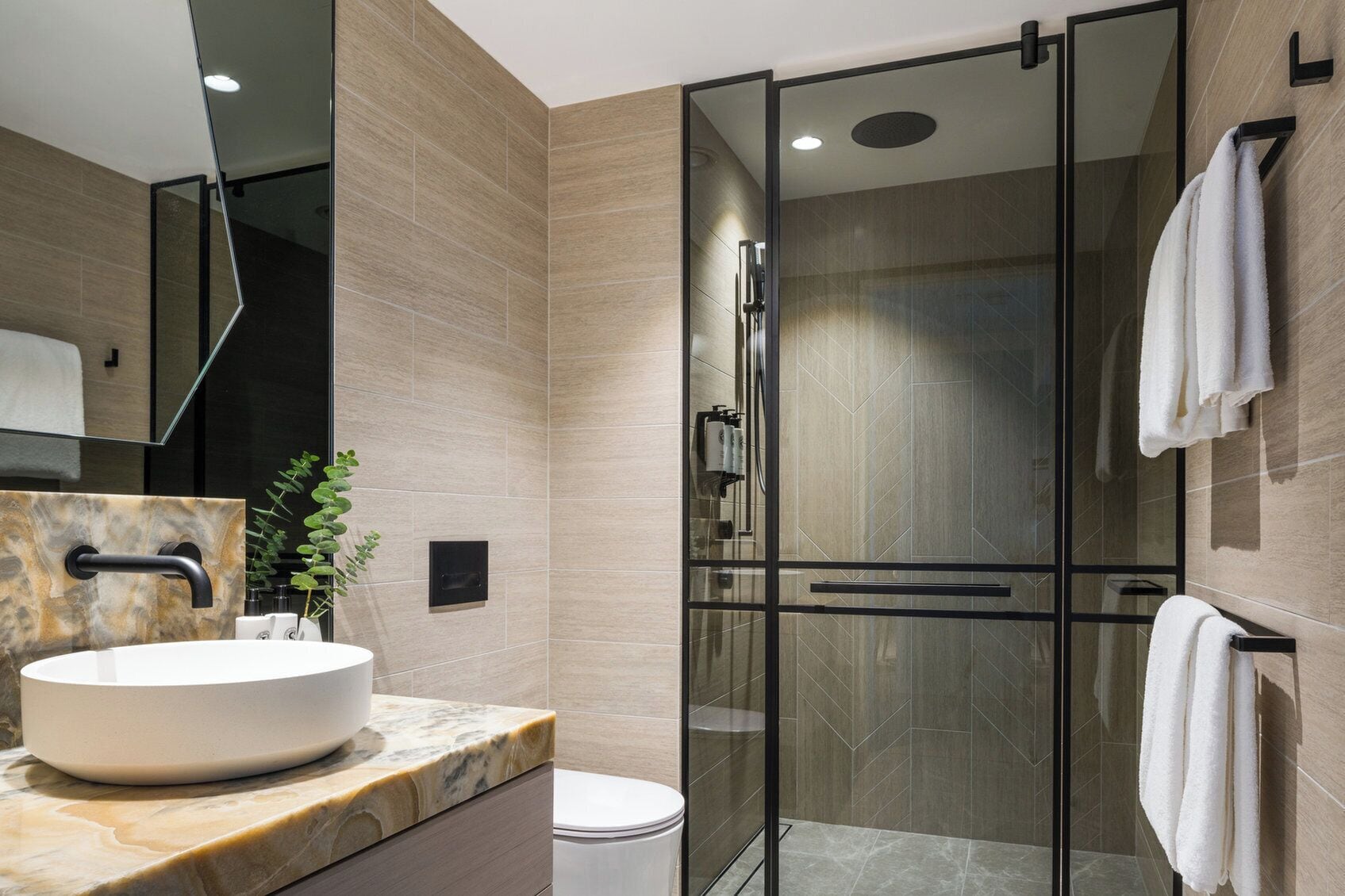 Un baño moderno con ducha envuelta en vidrio, lavamanos de mármol y retrete.