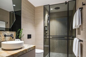 Un baño moderno con ducha envuelta en vidrio, lavamanos de mármol y retrete.
