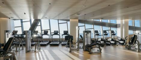 Un gimnasio con cintas de correr, elípticas y estaciones de pesas dispuestas en filas.