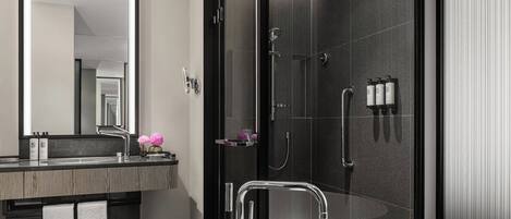 Un baño moderno con un espejo grande, una bañera independiente, una ducha con mampara de vidrio y un mueble de tocador con encimera oscura y dos toallas.
