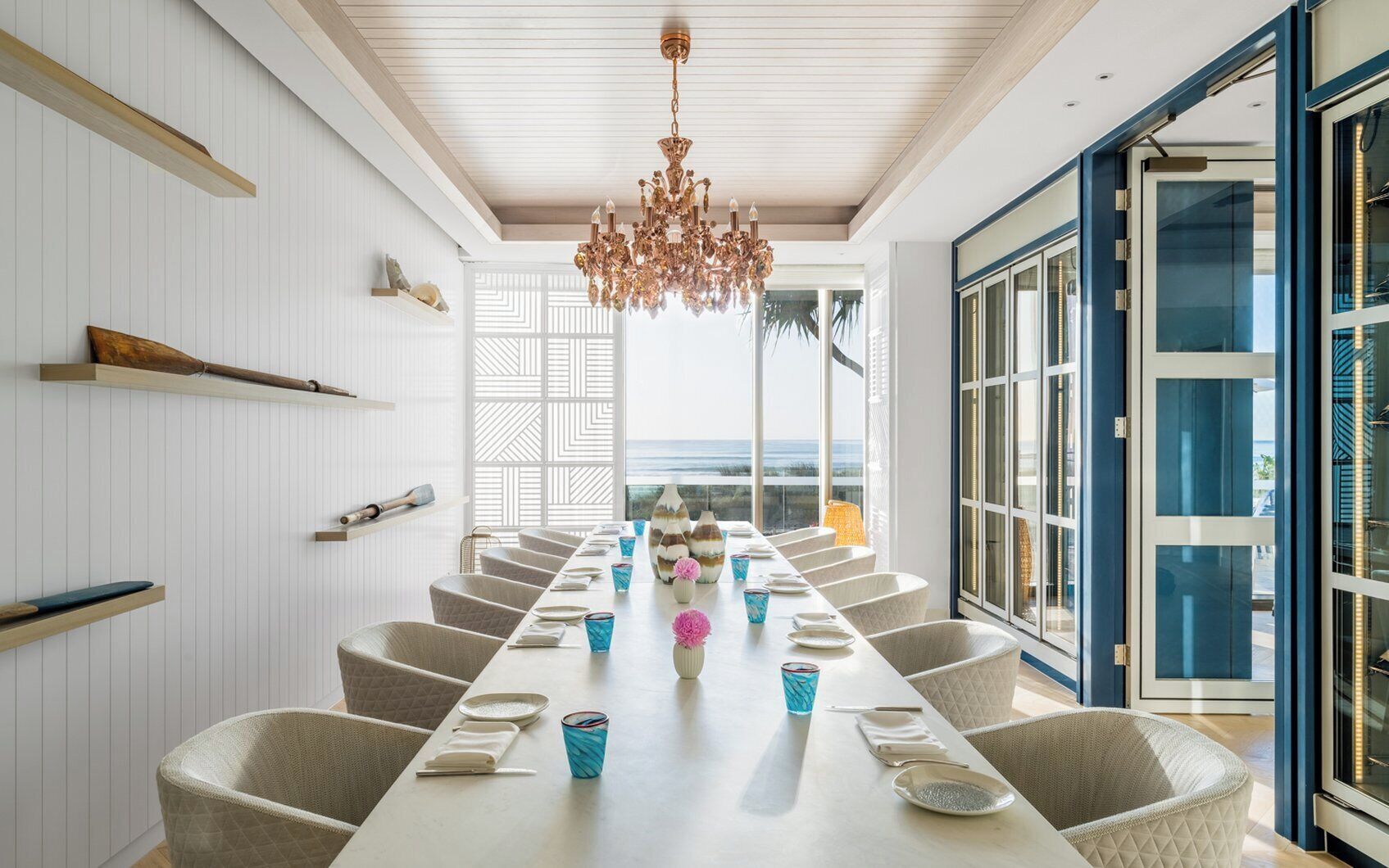 A dining area with a long table, chairs, and a chandelier.