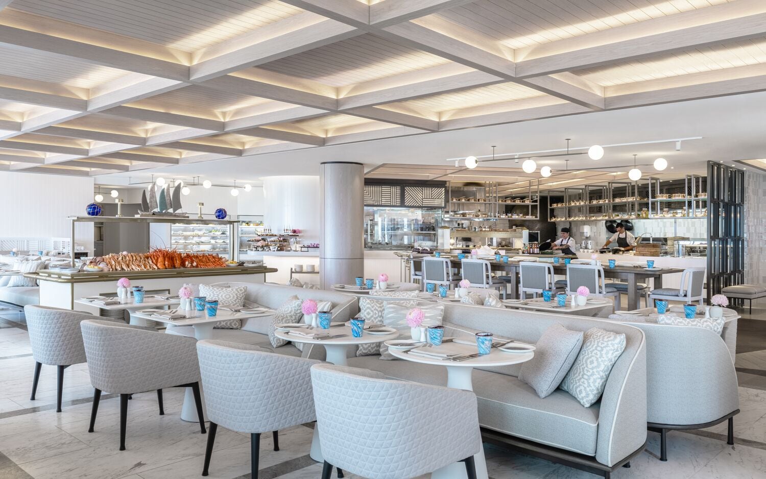 A modern restaurant with a high ceiling, seating areas, and a visible kitchen area.