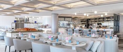 A modern restaurant with a high ceiling, seating areas, and a visible kitchen area.