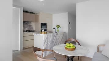 A modern kitchen with a marble island, wooden chairs, and a table with a bowl of apples.