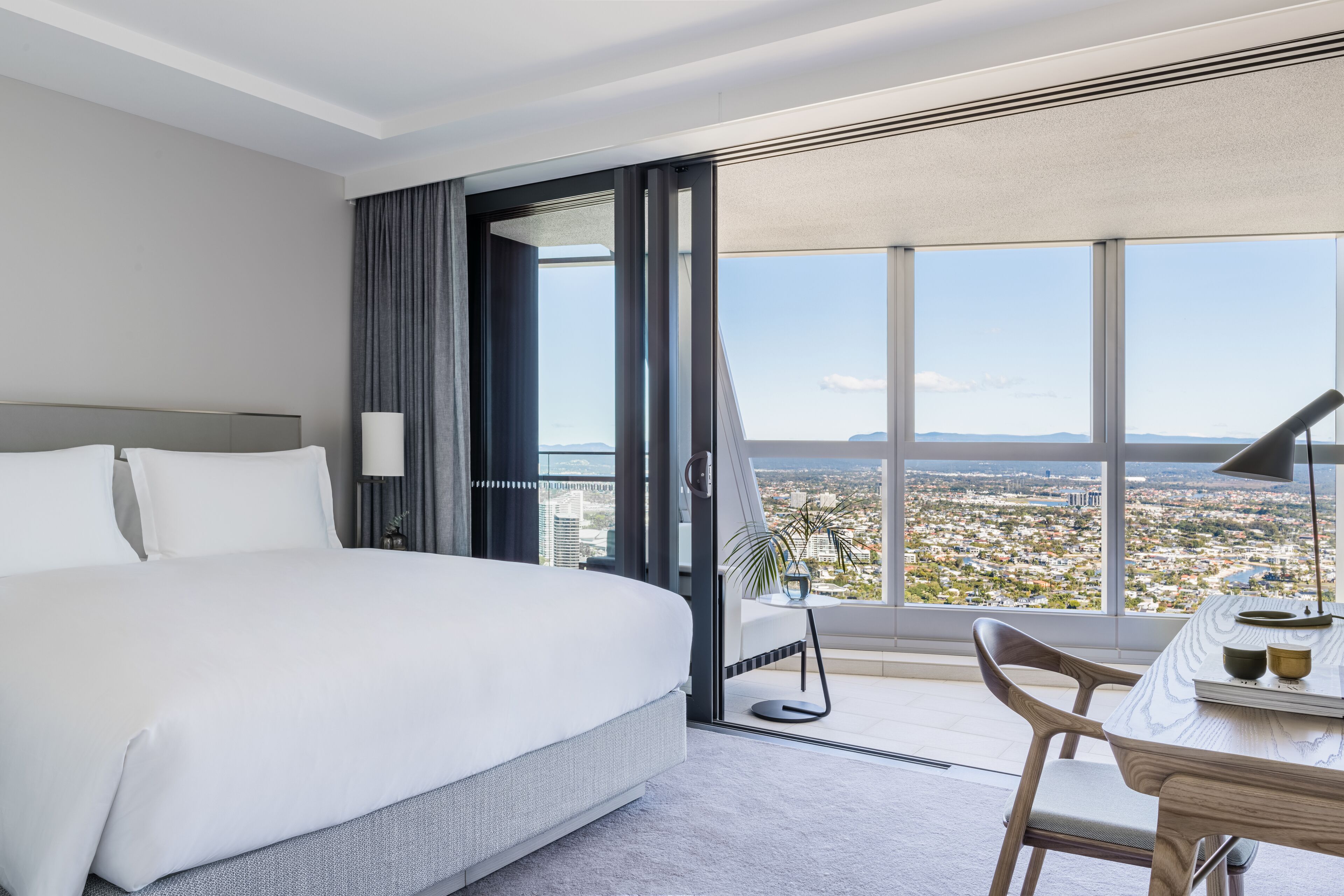 Une chambre d’hôtel moderne dotée d’un grand lit, d’un bureau avec une chaise et offrant une vue sur la ville grâce à de grandes fenêtres.