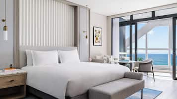 A modern hotel room with a large bed, a bench, a desk, and a view of the ocean.