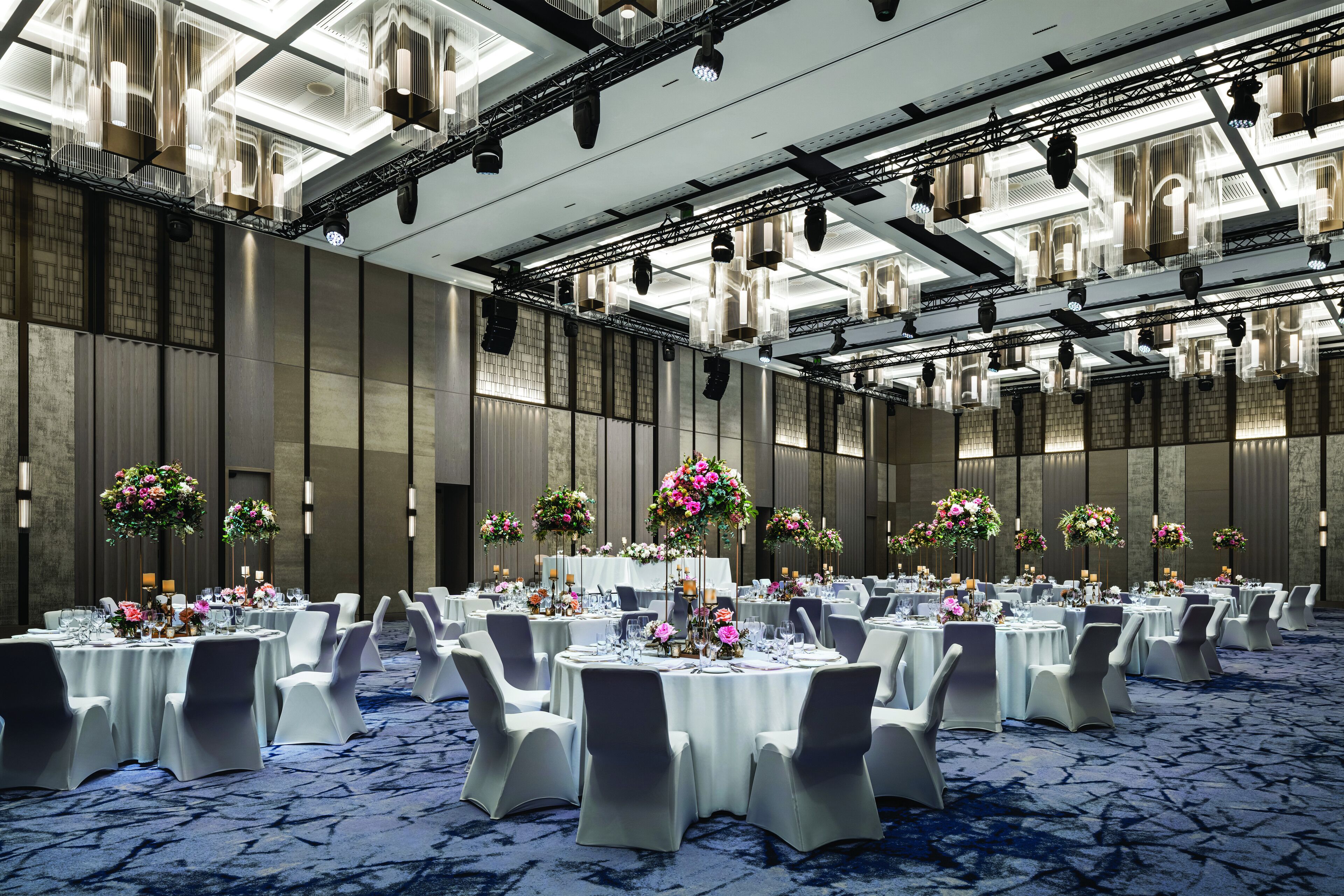 Un salón de banquetes con mesas redondas, sillas blancas y centros de mesa florales.
