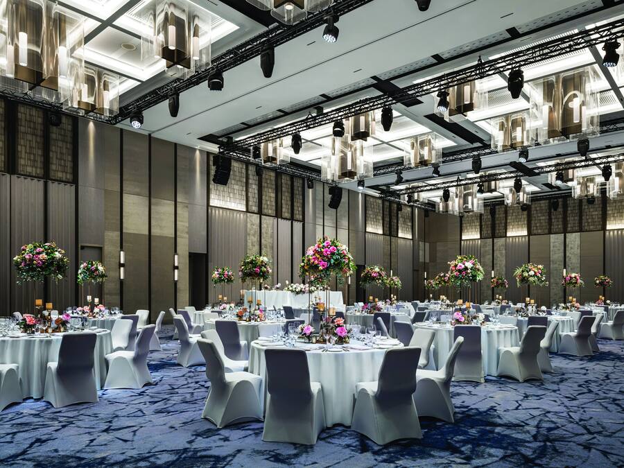 A banquet hall with round tables, white chairs, and floral centerpieces.